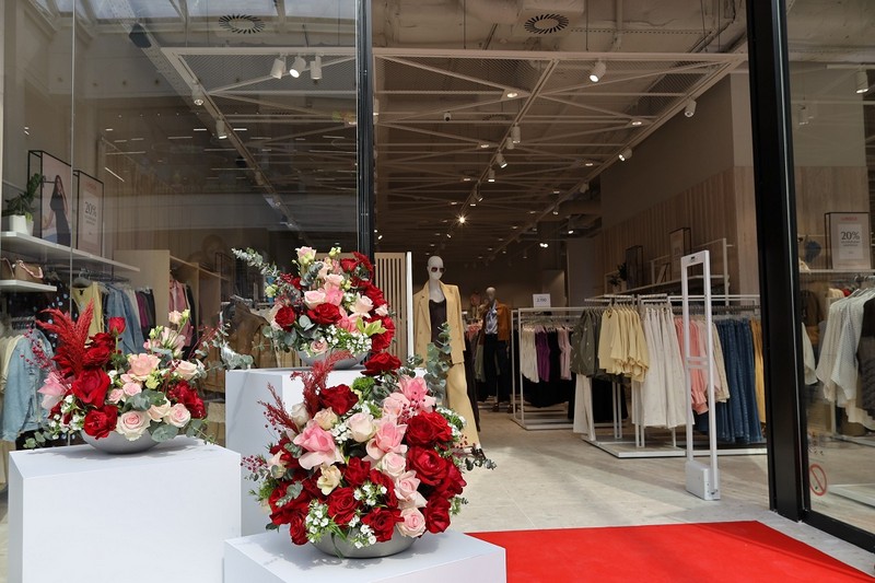 Otvaranje Lindex prodavnice u Galeriji Beograd uz cvetne aranžmane, crveni tepih i izloženu prolećnu kolekciju odeće u modernom enterijeru.