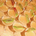 Čaše sa osvežavajućim napitkom od manga servirane na događaju, ukrašene kriškama voća sa natpisom „MANGO“, postavljene na stolu u elegantnom ambijentu.