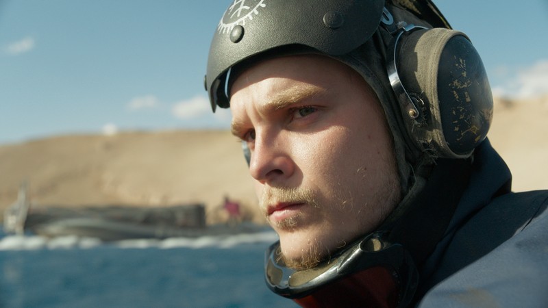 Glavni lik iz filma Gospodar Oluje sa zaštitnom kacigom posmatra more u postapokaliptičnom okruženju