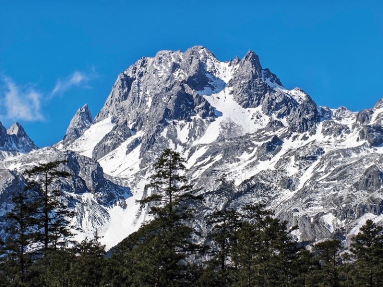 Visoka snežna planina sa stenovitim vrhovima i borovima u podnožju pod vedrim nebom, primer prirodne pejzažne fotografije