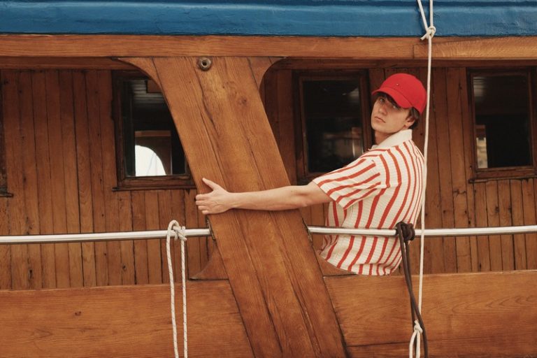 Jakov Jozinović u ležernoj letnjoj modnoj kombinaciji na brodu tokom Fashion&Friends kampanje, sa crvenim kačketom i prugastom majicom.