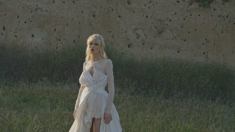 Nevena Božović u beloj haljini stoji u prirodi tokom snimanja spota za pesmu „Akvarel“
